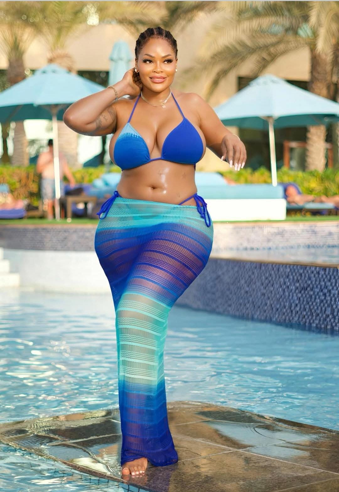 Woman in a blue bikini and colorful pants by a poolside.